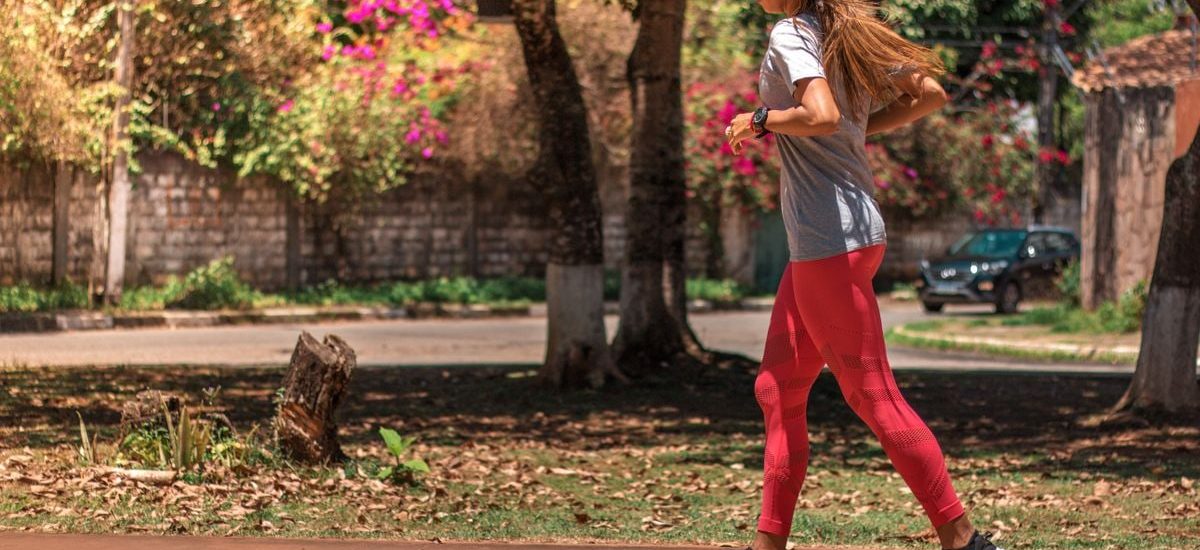 A woman jogs on a path surrounded by trees and vibrant flowers, embodying a healthy lifestyle.